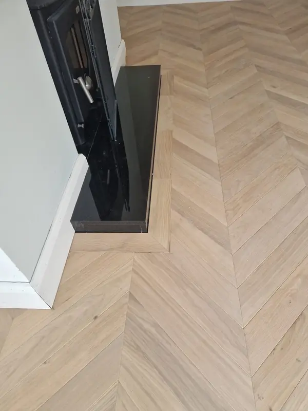 Pale herringbone oak flooring meeting a dark fitted unit and staircase