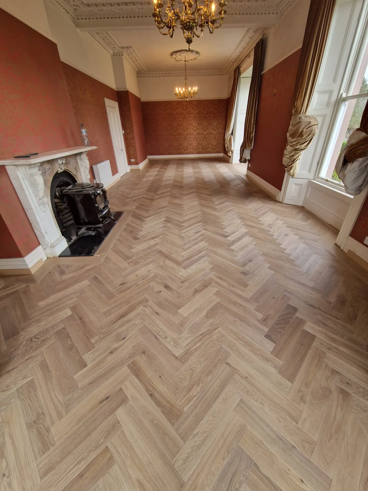 Herringbone parquet in a period room with a marble fireplace and chandelier