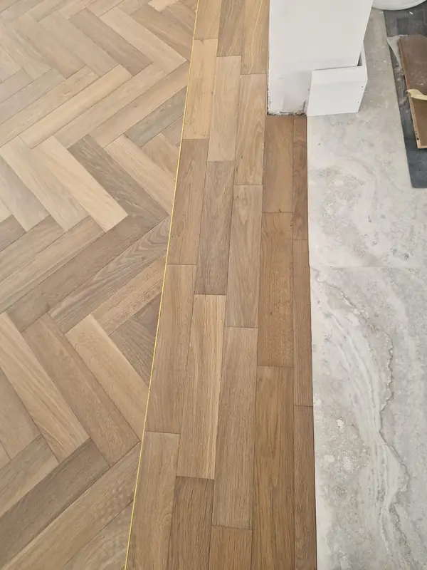Close detail of herringbone flooring meeting stone tile at a threshold