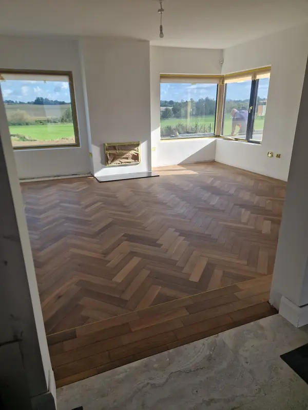 Deep-toned herringbone flooring in a bay-window living room with fireplace
